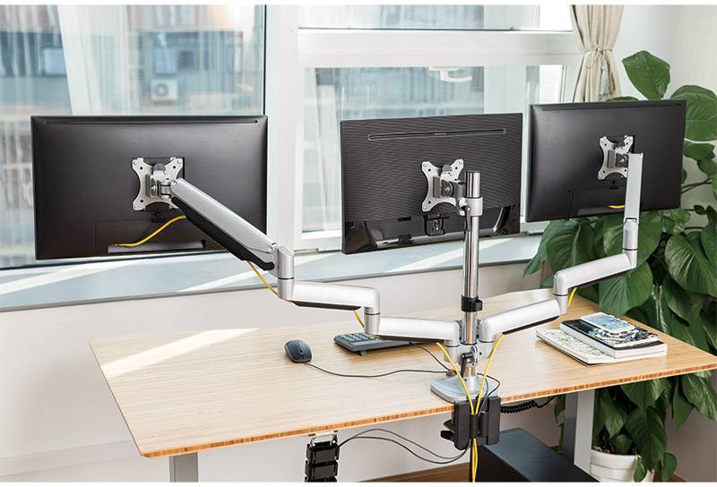 Twee monitoren op een in hoogte verstelbare bureauarm in een kantoor, met toetsenbord, muis en notitieboeken ernaast.