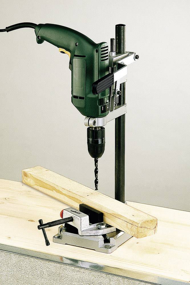 'Elektrische boormachine in een standaard die een houten plank op een bankschroef op een werkbank doorboort.'