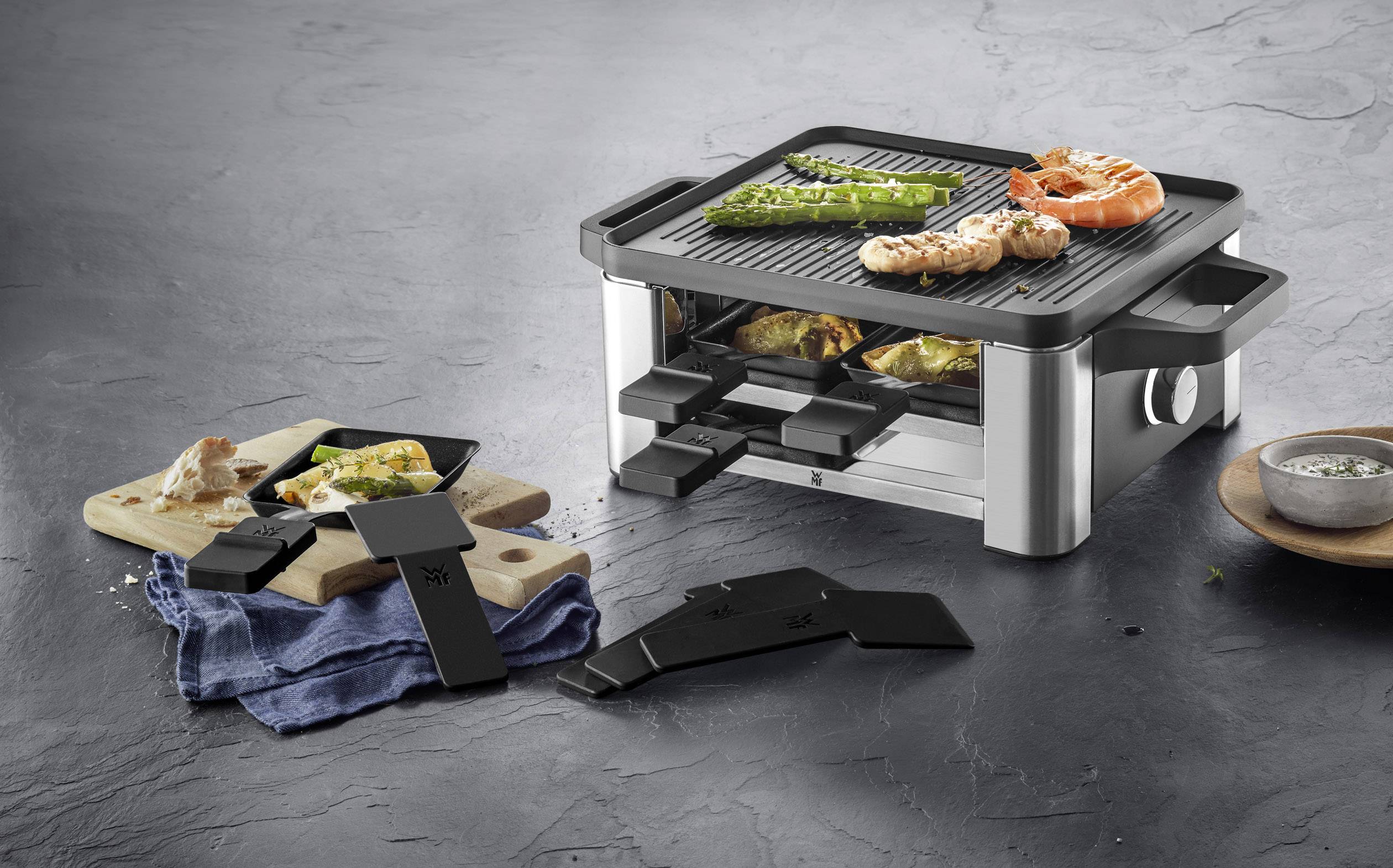 Een tafelgrill met een grilloppervlak bovenaan en meerdere pannetjes eronder, waarop groenten en zeevruchten kunnen worden bereid.