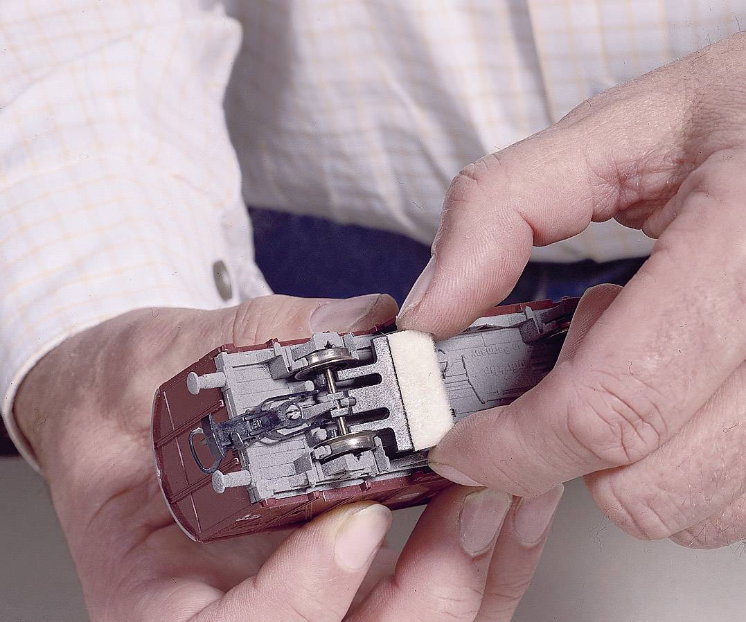 Een persoon houdt een modeltreinspeelgoed-prototype vast en verwijdert voorzichtig een minuscuul stuk spons van de onderkant met zijn vingers.