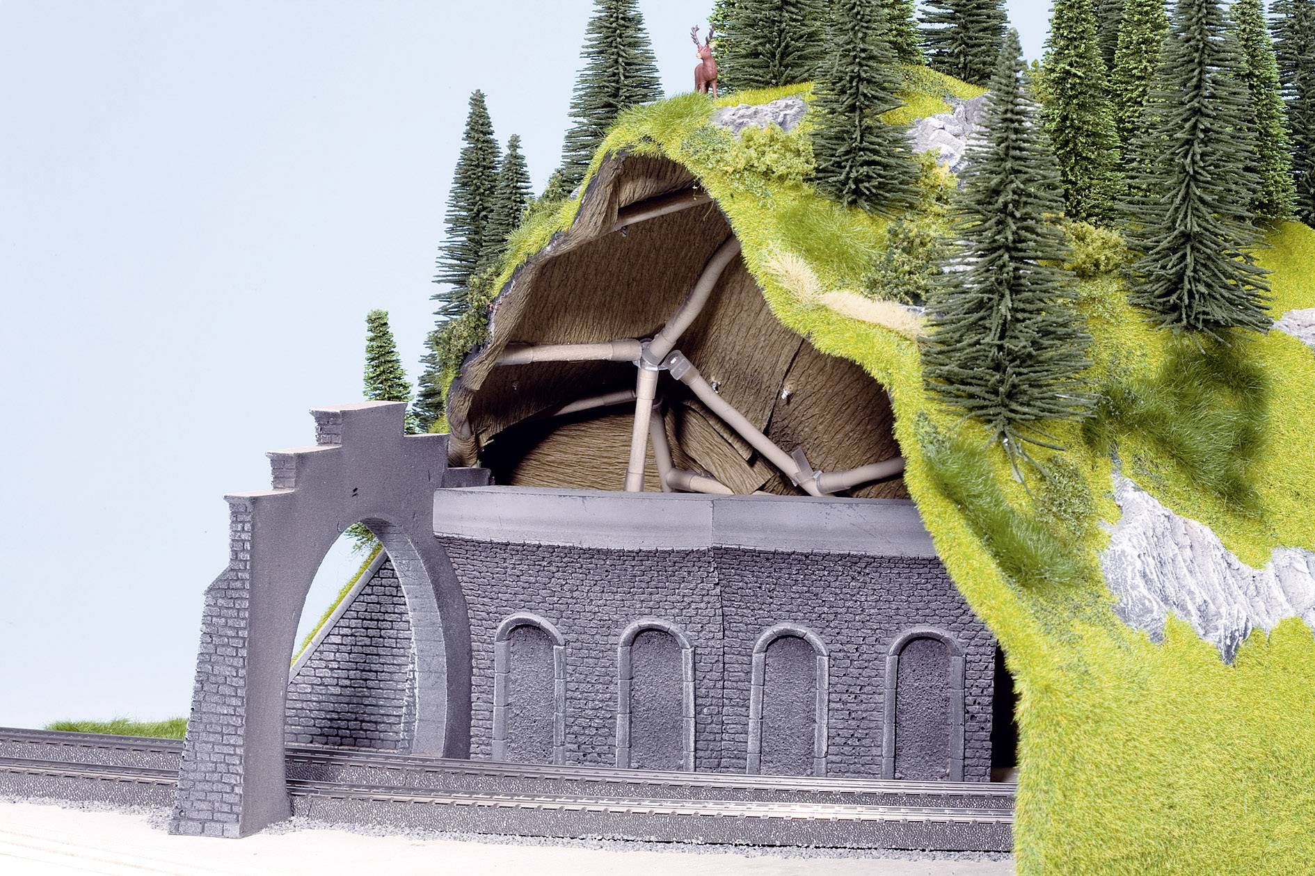 Een miniatuurmodel van een tunneluitgang toont een met groen begroeid heuvellandschap met bomen en een blootliggende houten tunnelconstructie.