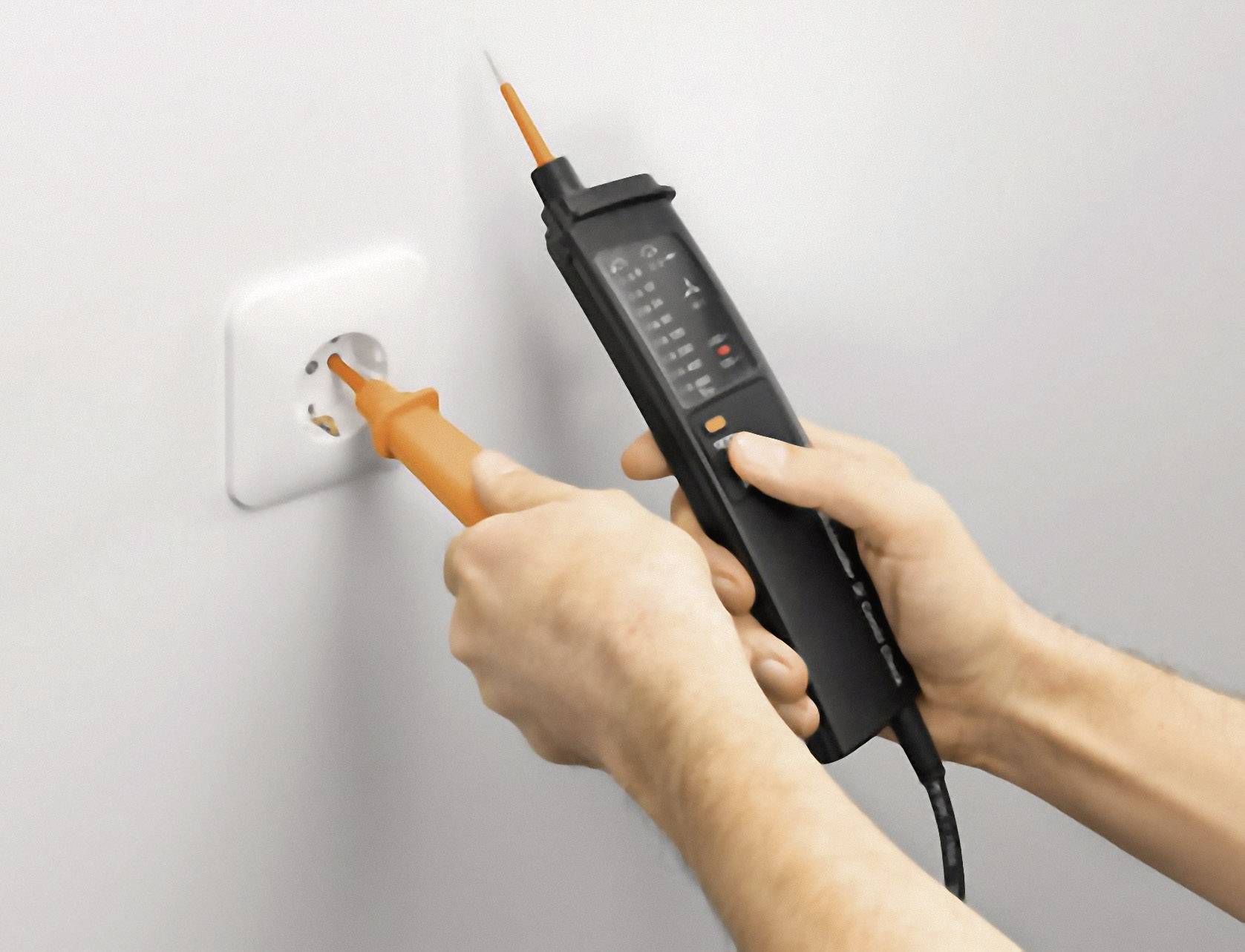 Een persoon test een stopcontact met een spanningzoeker. Hij/zij meet de spanning om de elektrische veiligheid te controleren.