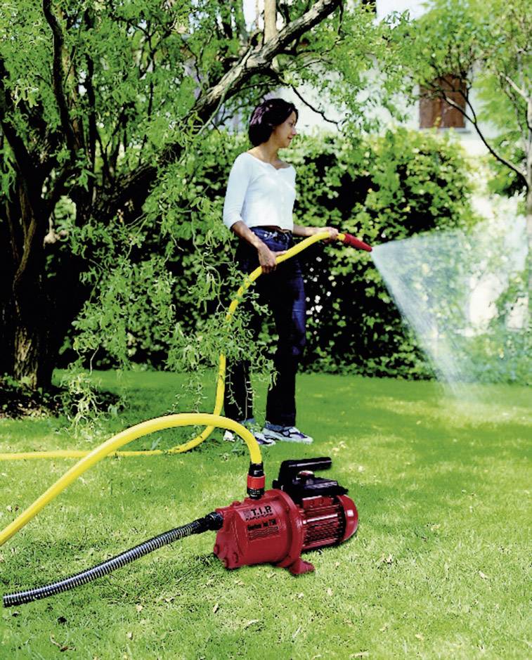 Een persoon begiet een gazon met een gele slang die is aangesloten op een rood gekleurde waterpomp.