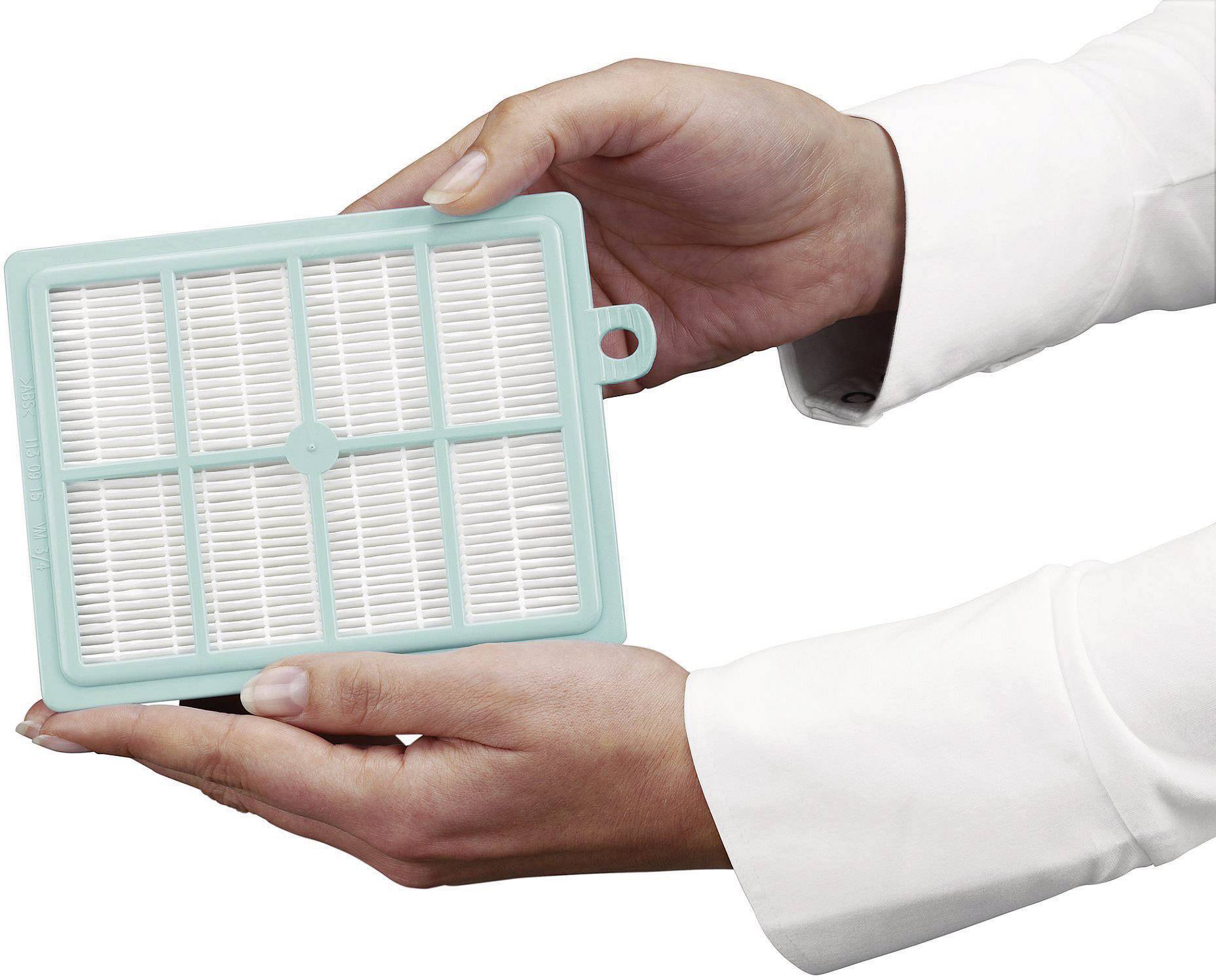 Twee handen houden een rechthoekige luchfilter met witte plooien in een turquoise frame. De filter lijkt nieuw te zijn.