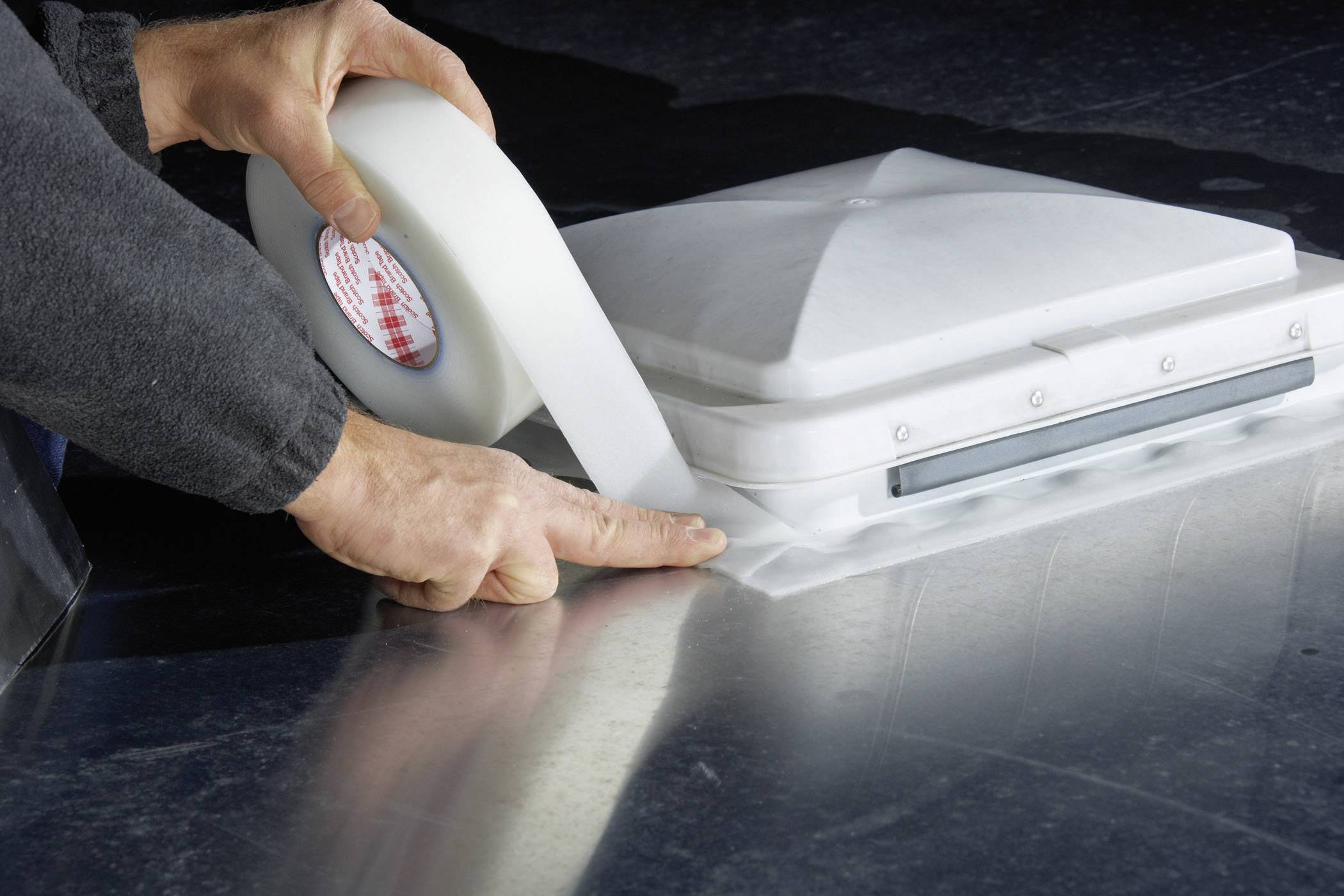Een persoon dicht een ventilatieopening op een dak af met een wit afdichtband om waterlekken te voorkomen.