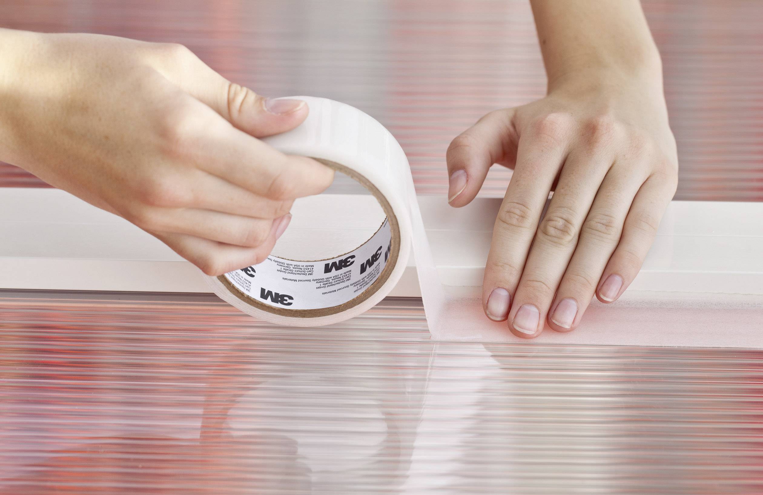 Twee handen plakken een transparante plakband op een reflecterende oppervlakte. De tape wordt strak en nauwkeurig aangebracht.