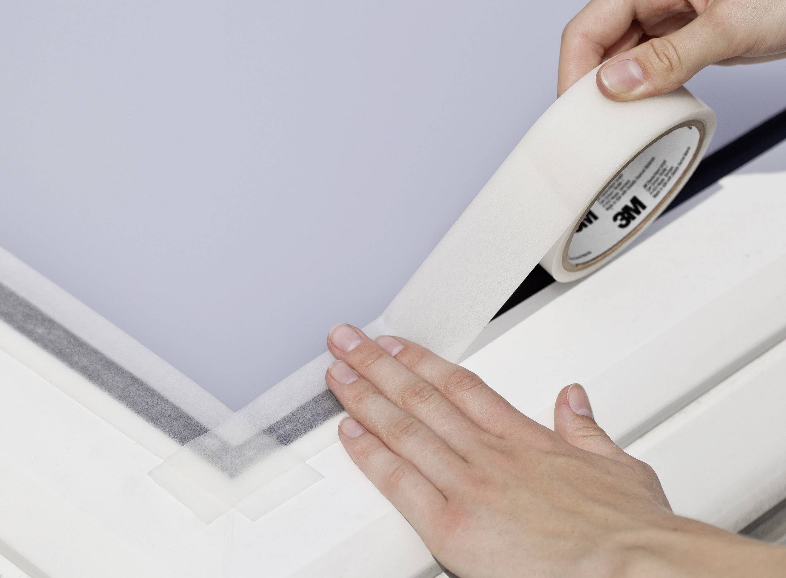 Hand brengt plakband aan op een vensterlijst om de afdichting te verbeteren. Close-up toont het etiket van de rol en zorgvuldig aanbrengen.