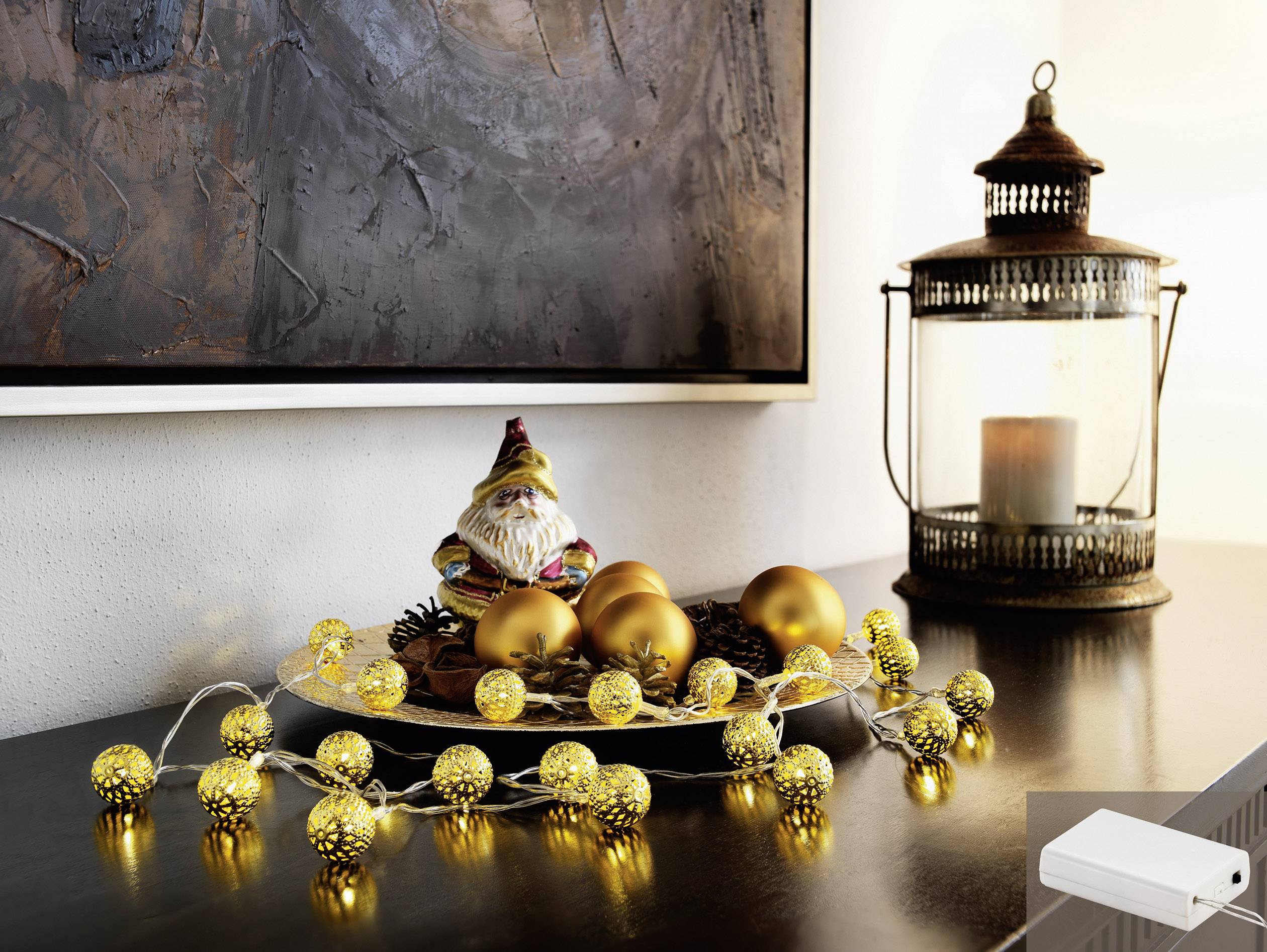Een decoratieve tafel met gouden kerstballen en een lichtsnoer, naast een lantaarn en een kleine kerstfiguur.