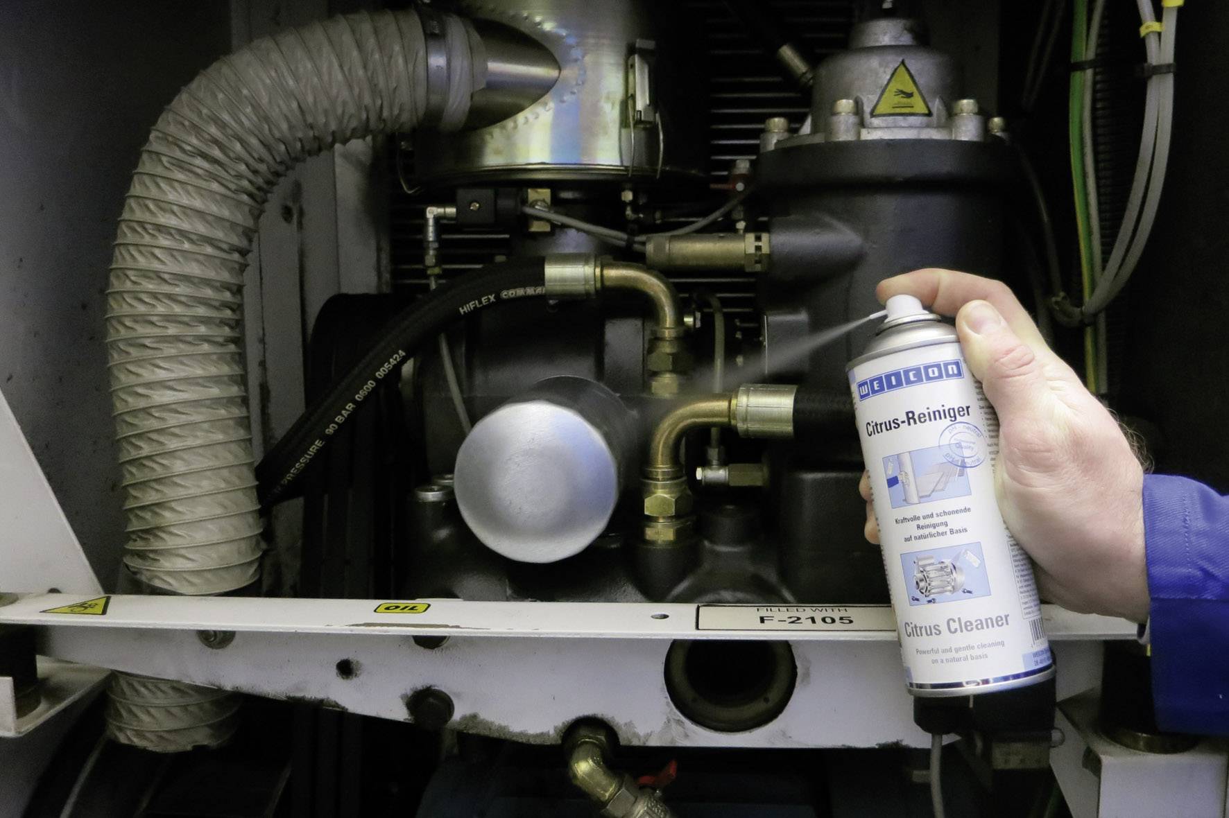 Een persoon houdt een blik gasreiniger voor een machine met slangen en buizen. De scène toont het reinigingsproces.