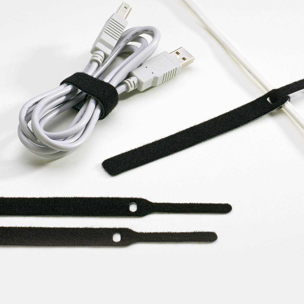 Klittenband kabelbinders naast een opgerolde USB-kabel; illustreren hoe kabels georganiseerd kunnen worden.
