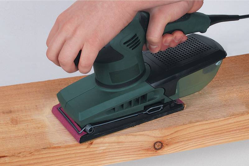 Een hand houdt een elektrische slijpmachine vast die een houten plank bewerkt om het oppervlak glad te maken.