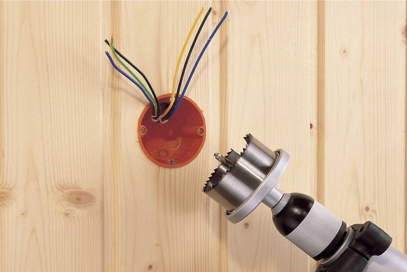 Een elektriciteitsverdeelkast met uitstekende kabels en een boormachine aan een houten muur.