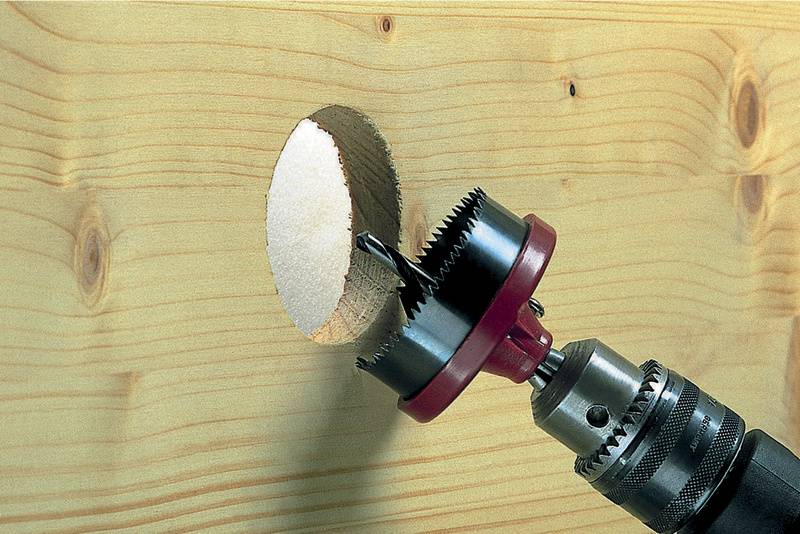 Boor met gatenzaag snijdt een rond gat in een houten plank.