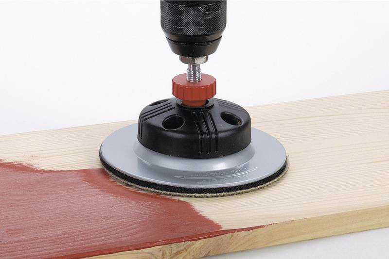 Een slijpmachine met een ronde opzetstuk slijpt rode verf van een houten plank.