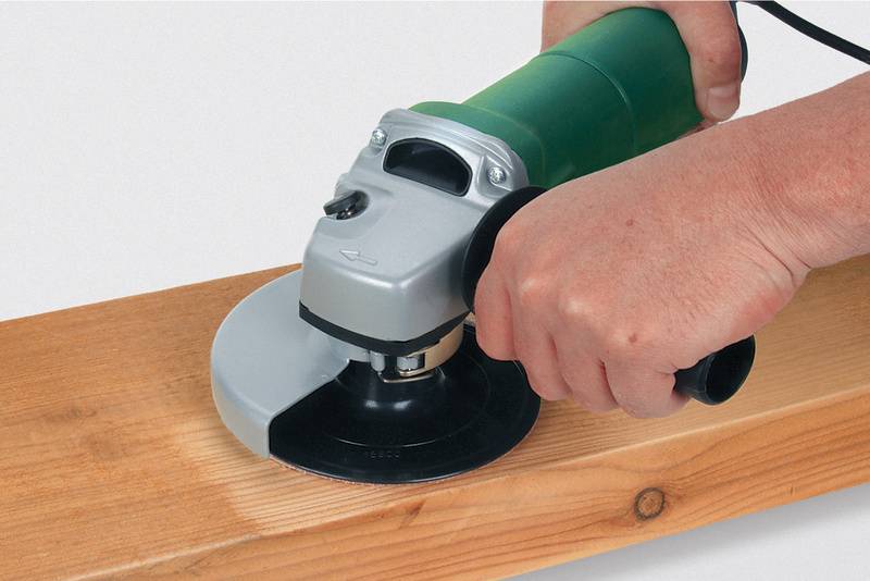 Een hand gebruikt een haakse slijper om het oppervlak van een houten plank glad te maken.