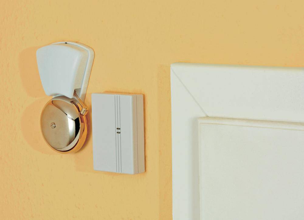 Een deurbel en een schakelaar aan een oranje muur naast een witte deurpost.