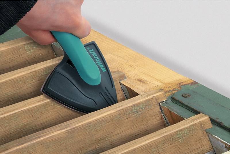 Een hand gebruikt een gereedschap met groene handgreep om de rand van houten lamellen te schuren.