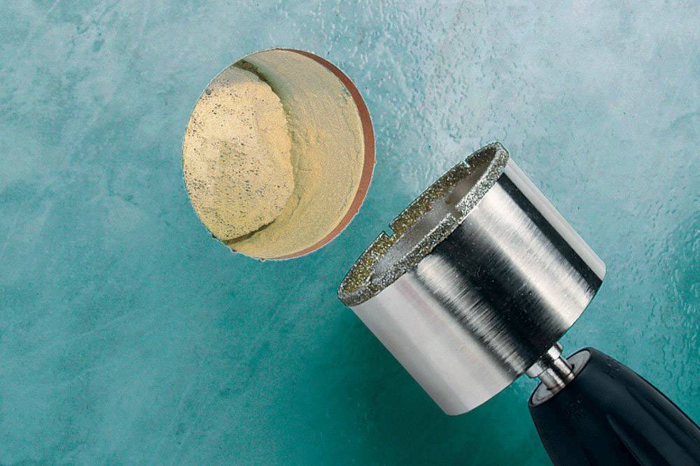 Een metalen boor snijdt een gat in een gladde blauwe oppervlakte, waarbij een schijfvormig stuk materiaal wordt uitgehaald.