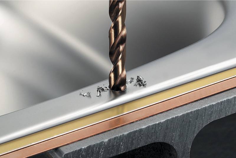 'Close-up van een boorpunt die een metalen stuk boort, met metaalspanen rondom de boorlocatie.'