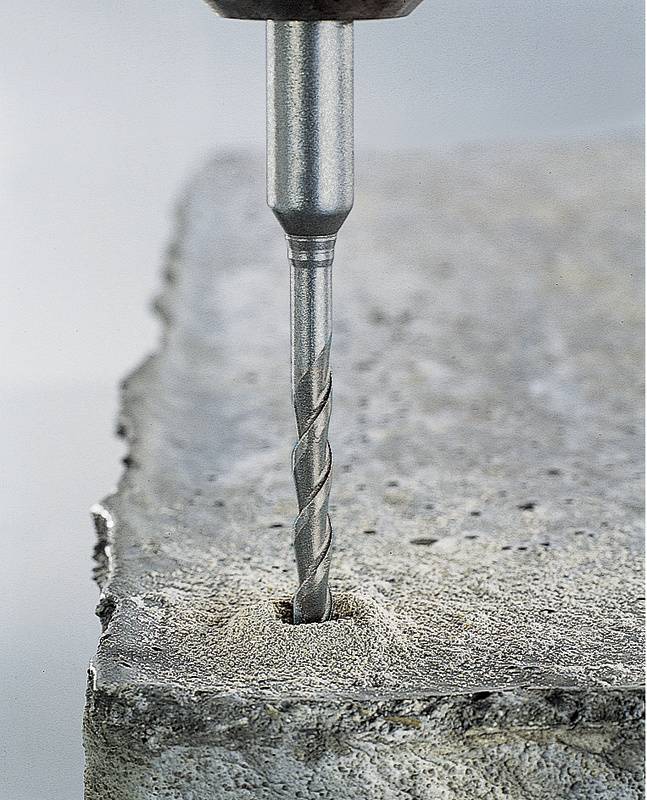Een boor boort een gat in een betonblok. De boor is van metaal en heeft spiraalvormige groeven.