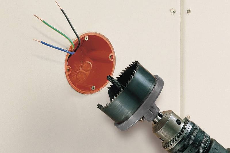 Boormachine maakt een ronde opening in een muur om een inbouwdoos te plaatsen waaruit kabels steken.