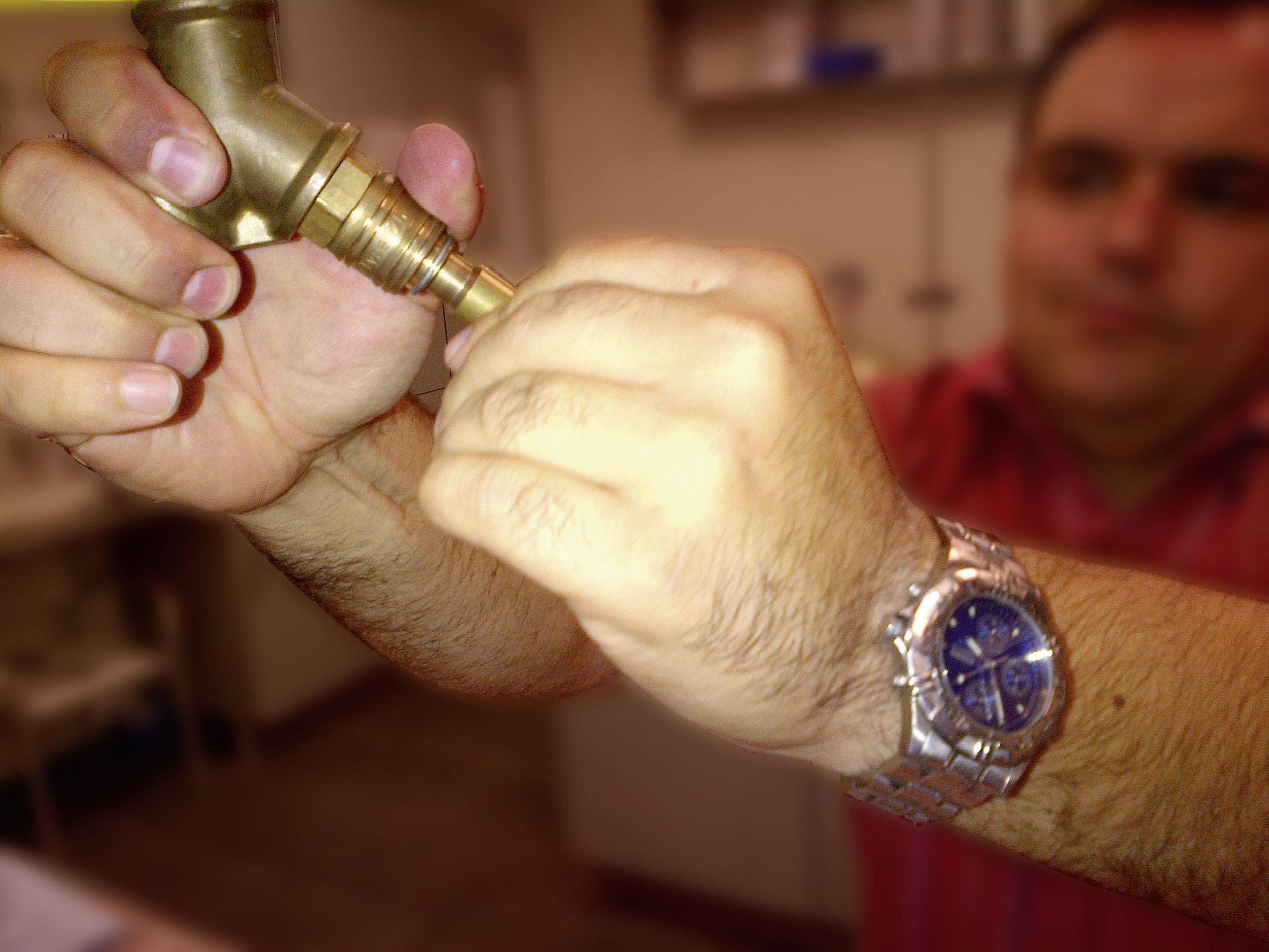 Een persoon repareert een waterkraan door het ventiel aan te draaien. Hij draagt een zilveren horloge om zijn pols.