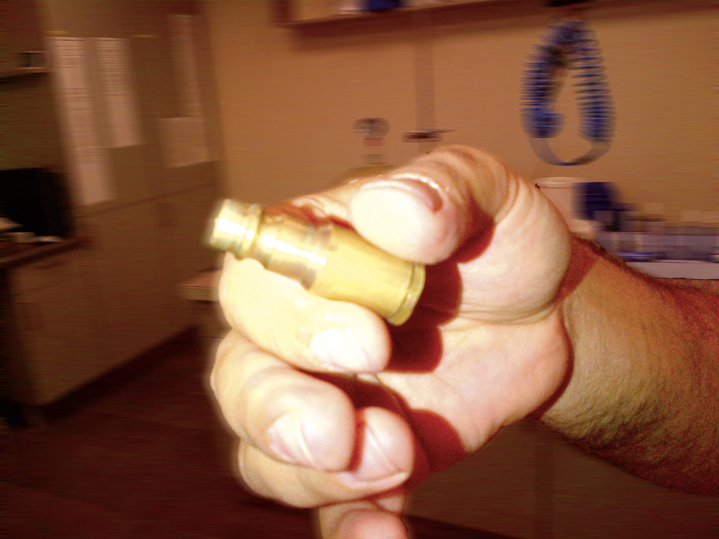 Een hand houdt een kleine metalen cilinder vast in een laboratoriumomgeving. De achtergrond is wazig.