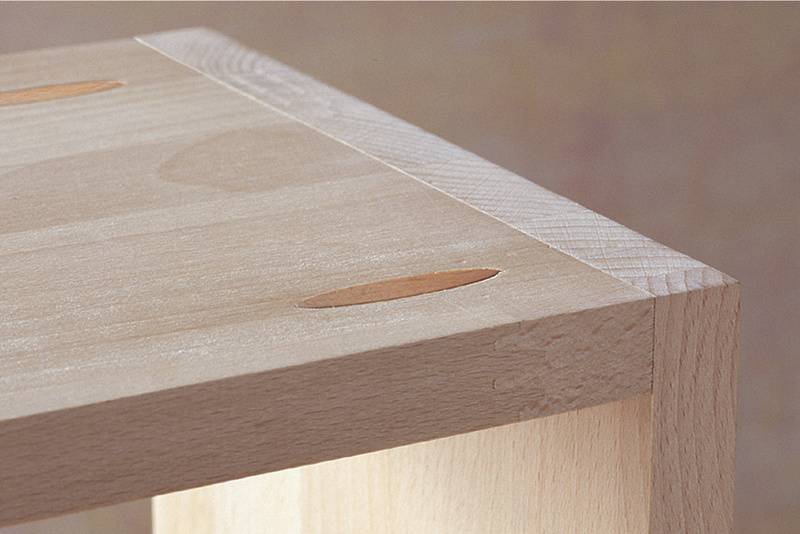 Hoek van een houten tafel met zichtbare penverbindingen.