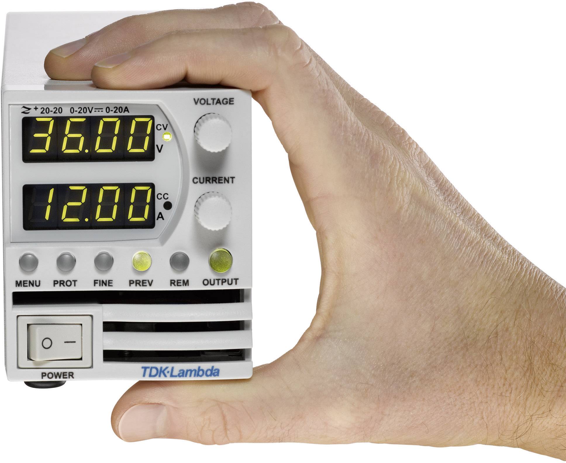 Hand houdt een elektronisch apparaat vast met een digitaal display. Bovenaan staat '36,00' volt, onderaan '12,00' ampère. Merknaam 'TDK-Lambda' zichtbaar.