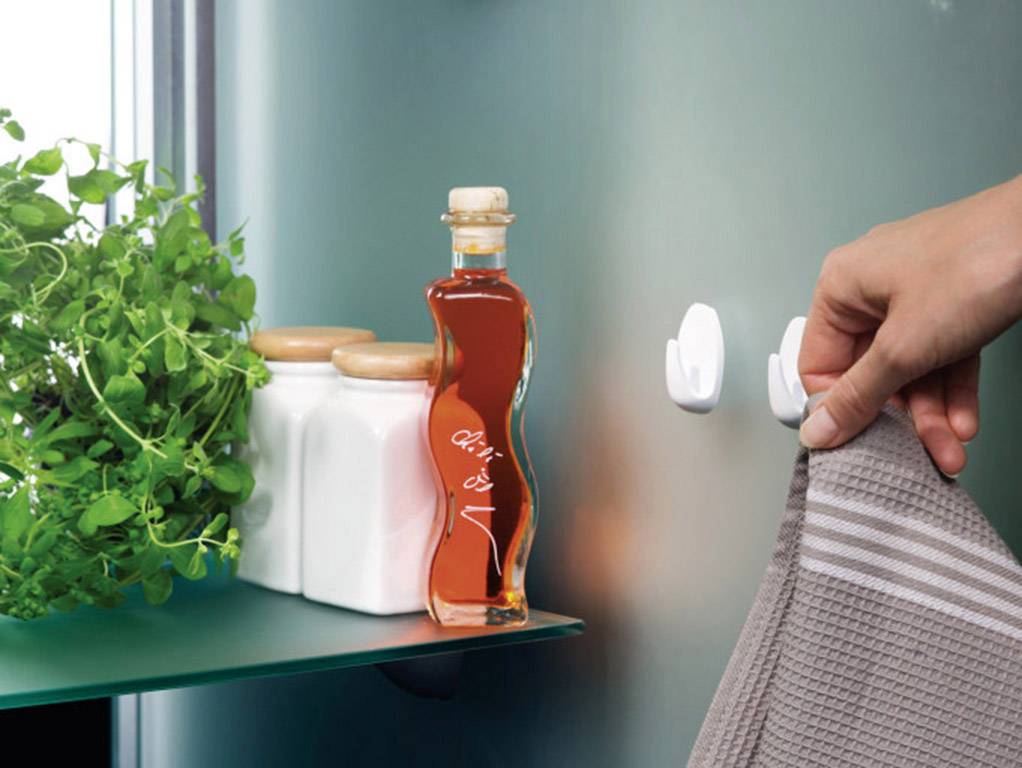 Een hand hangt een grijs handdoek aan een haak. Ernaast staan kruidentopjes en een fles met olie op een plank.