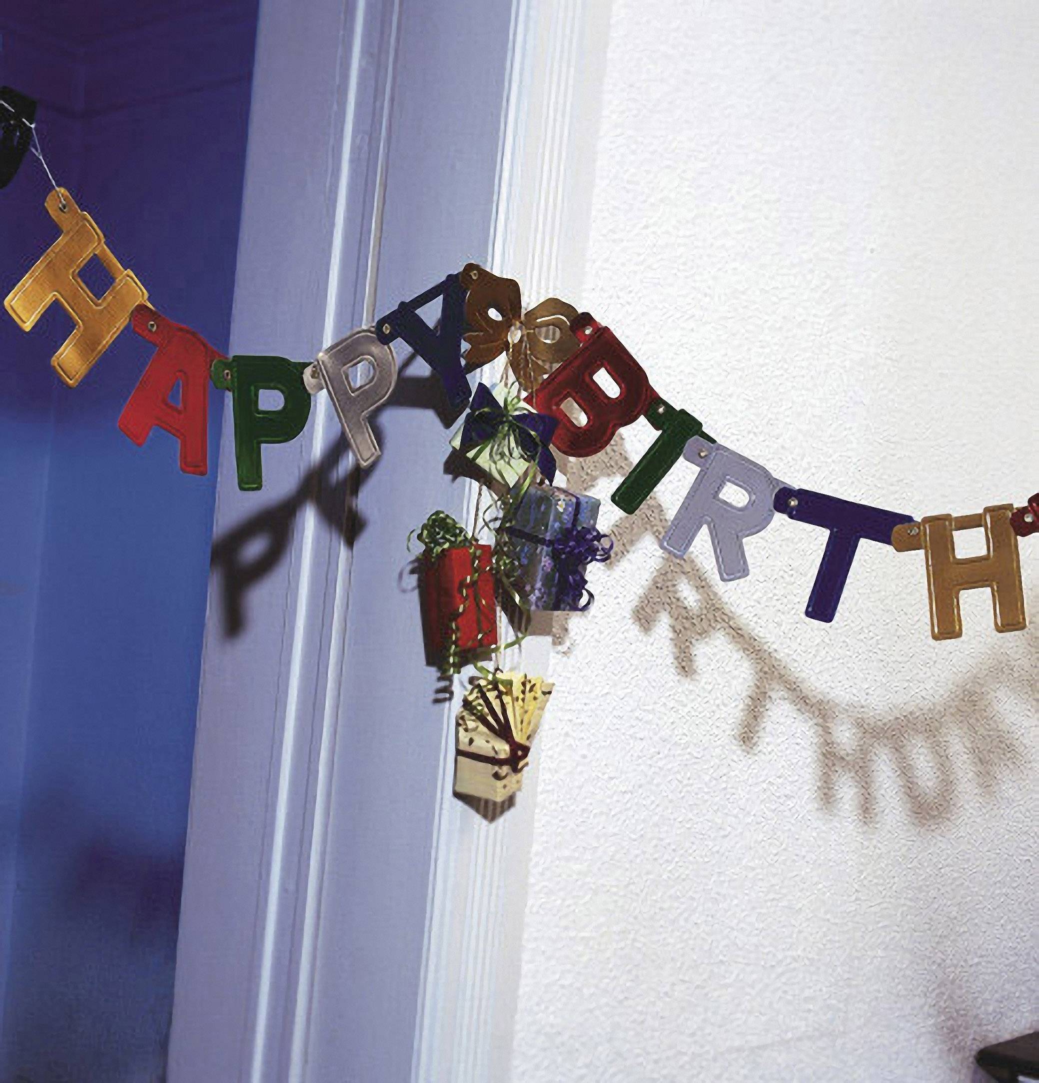 Spandoek met kleurrijke letters die 'HAPPY BIRTHDAY' spellen, hangt diagonaal aan de muur. Op de achtergrond zijn schaduwen zichtbaar.