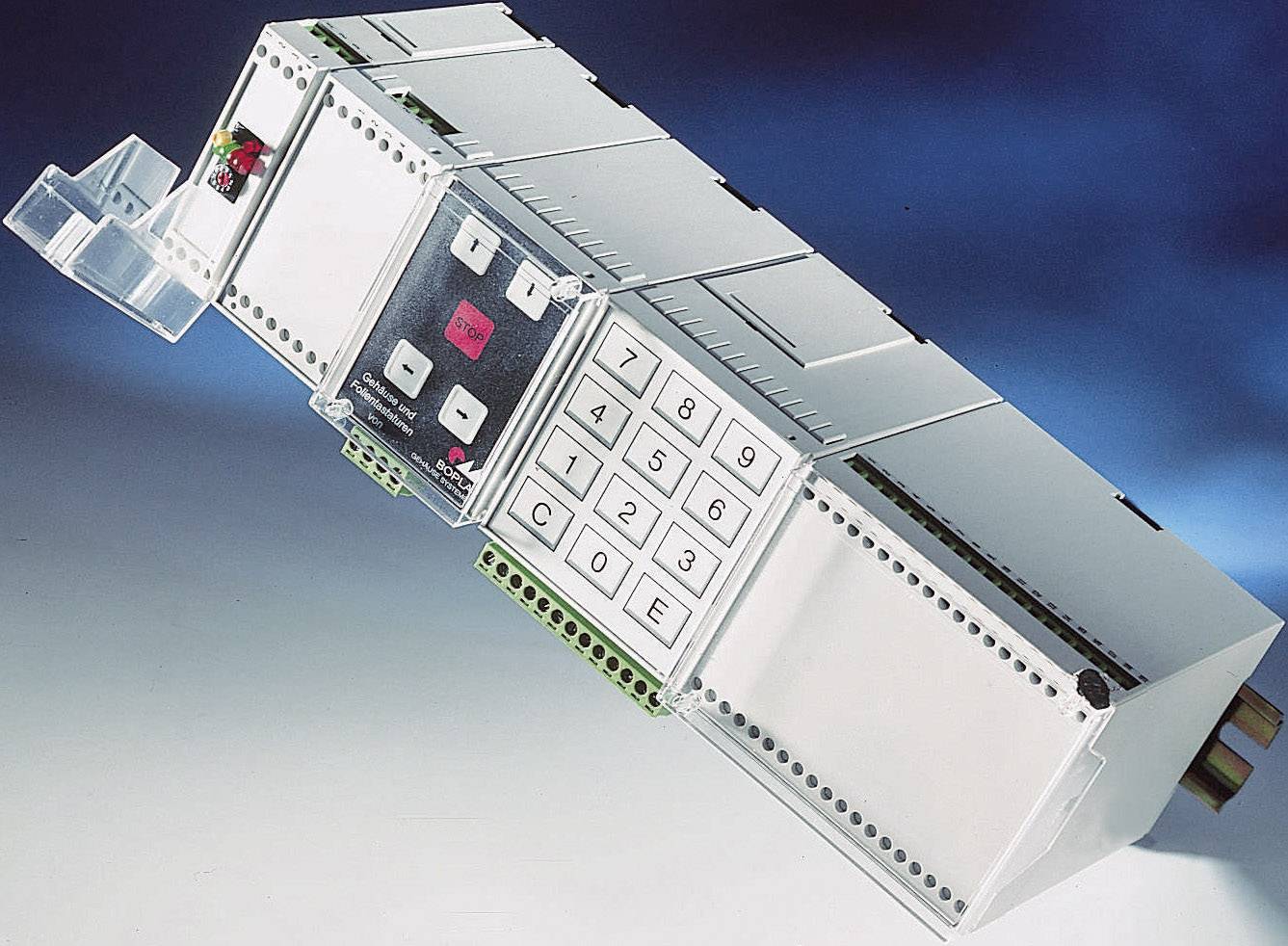 Een elektronisch apparaat met toetsenblok en digitale displays, gemonteerd op een DIN-rail, tegen een blauwe achtergrond.