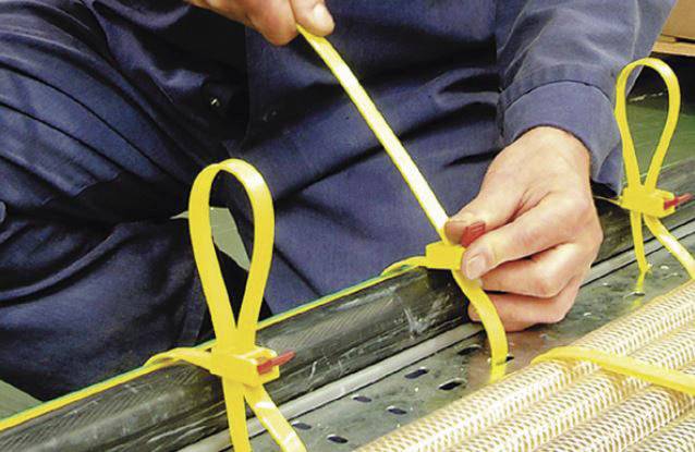 Een persoon trekt een geel band strak aan om een bundel te bevestigen. De focus ligt op nauwkeurig handmatig werk bij het verpakken of vastzetten.