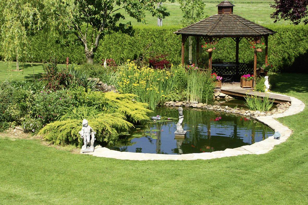 Een keurig onderhouden tuin met een vijver, omringd door groene planten en gele bloemen. Op de achtergrond staat een houten paviljoen.