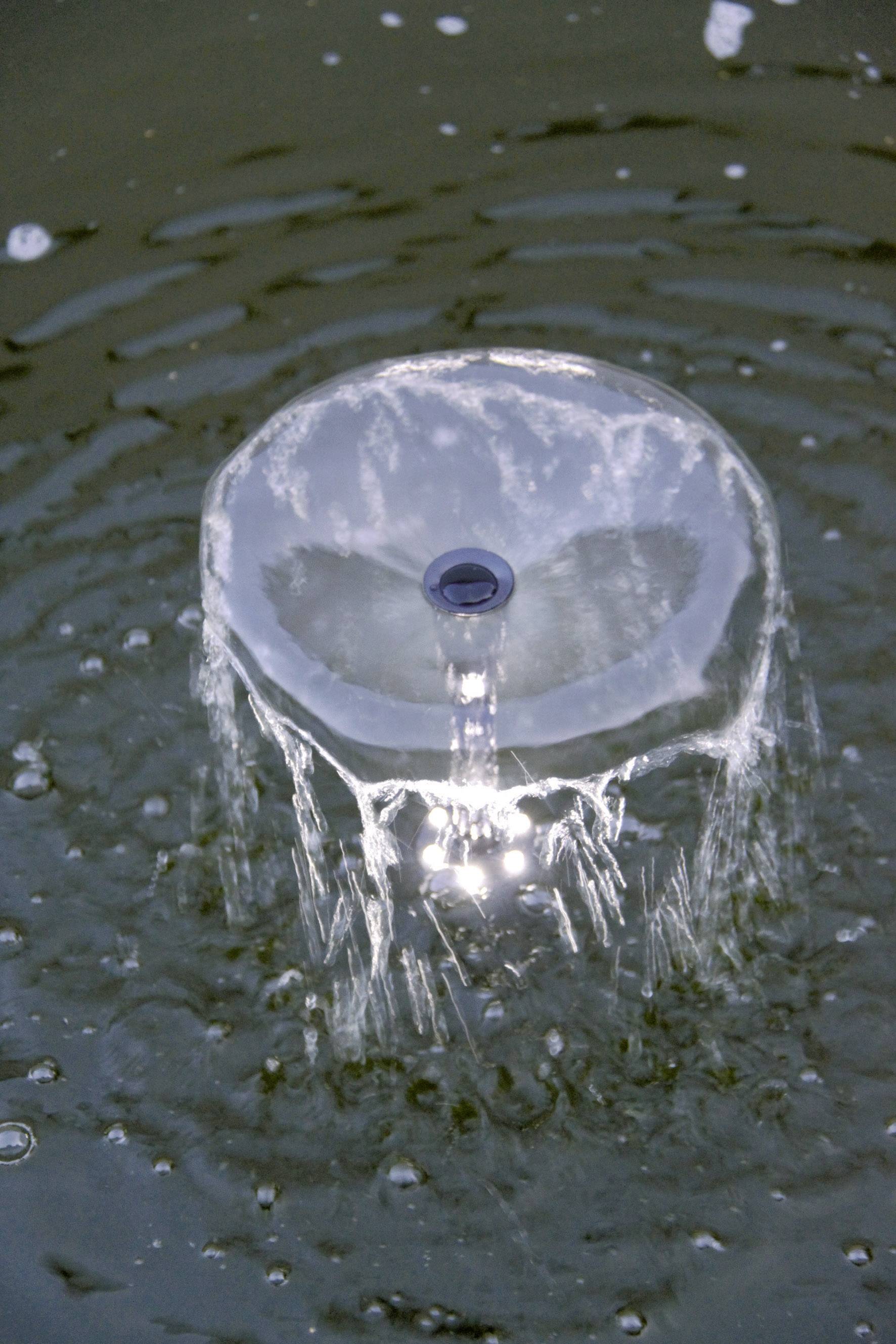 Een kleine fontein in het water creëert cirkelvormige golven om zich heen. Het water bruist zacht vanuit een centraal punt.