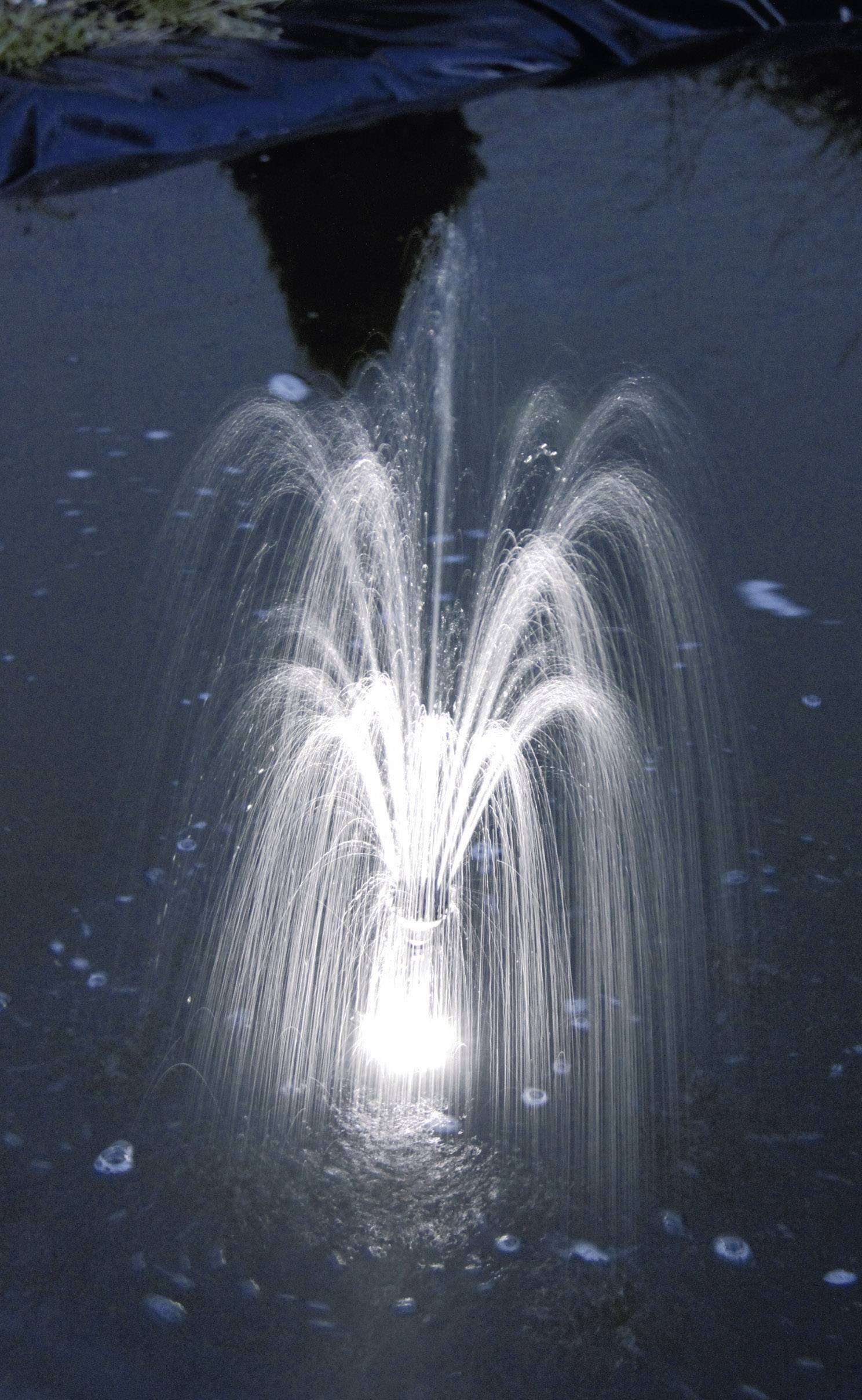 Een verlichte fontein spuit water in een donkere vijver, het licht creëert een stralend effect op de waterstralen.