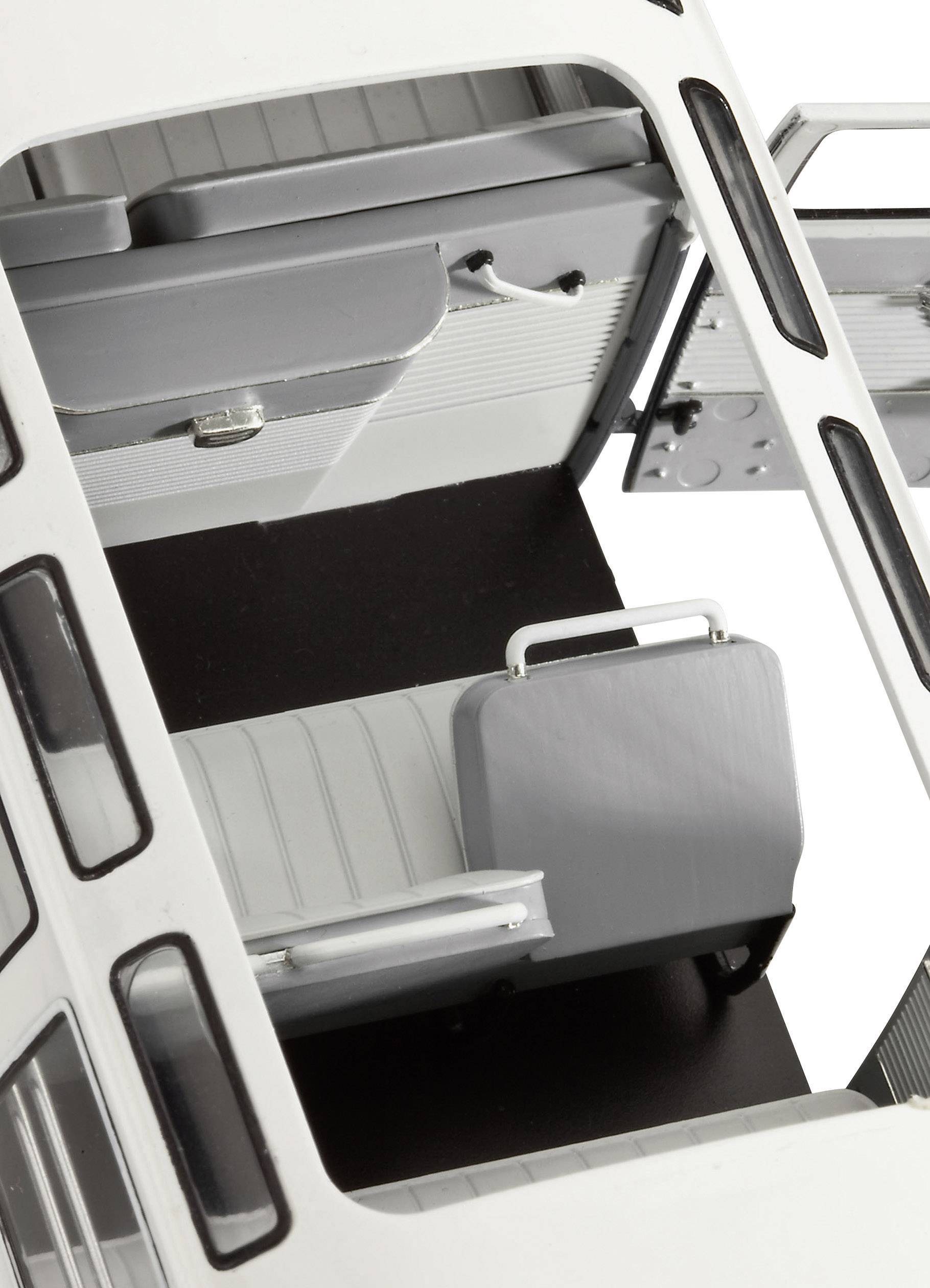 Het beeld toont het interieur van een model van een bus of camper, met grijze en witte stoelen en een openstaande deur.