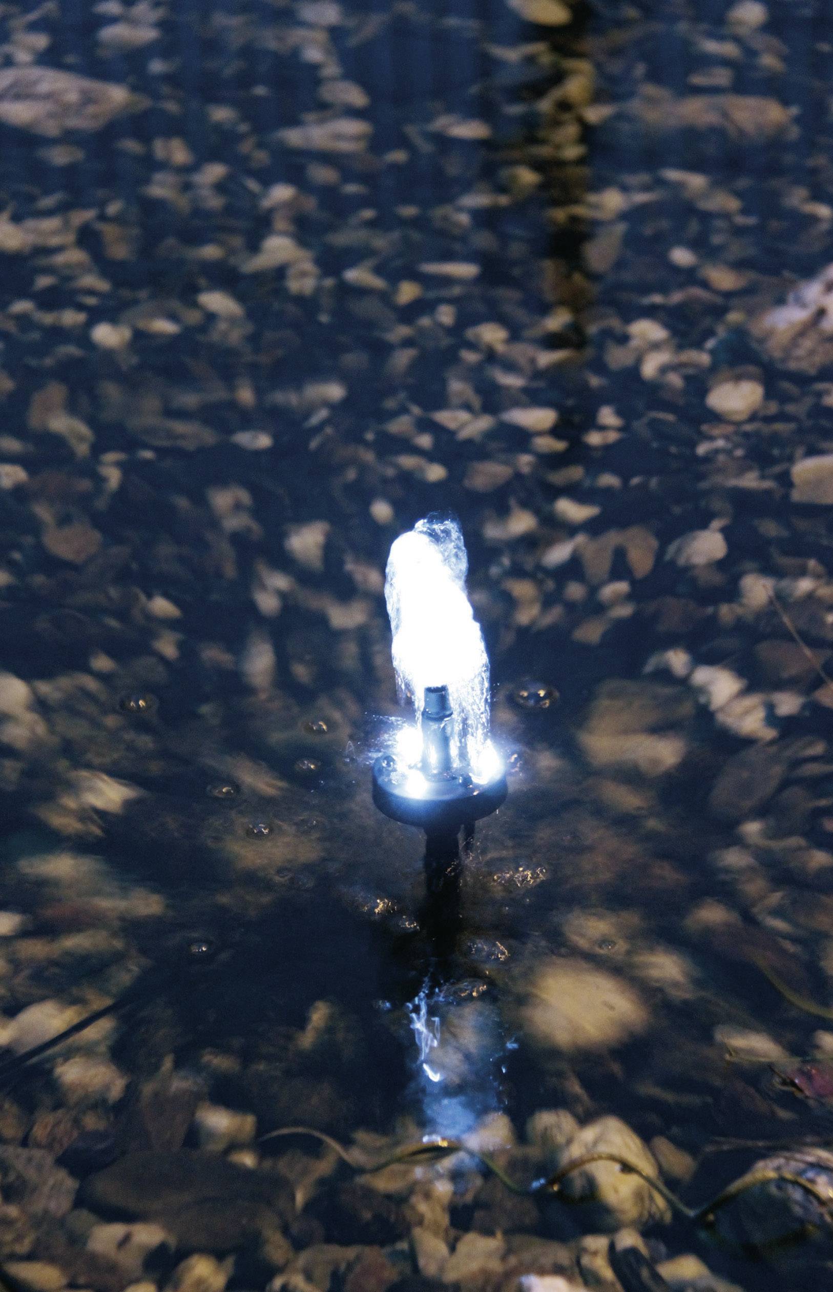Kleine watersproeier bruist in een vijver met kiezels. Subtiel licht verlicht het spetterende water.