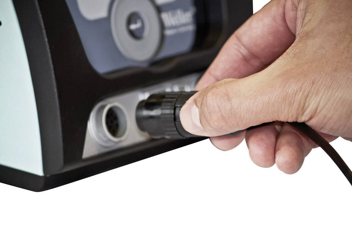 Een hand steekt een kabelstekker in een aansluiting op een elektrisch apparaat.