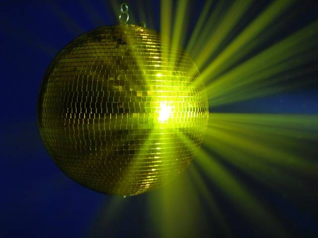 Een gouden discobal straalt geel licht in alle richtingen uit. De achtergrond is donkerblauw, wat de lichteffecten versterkt.