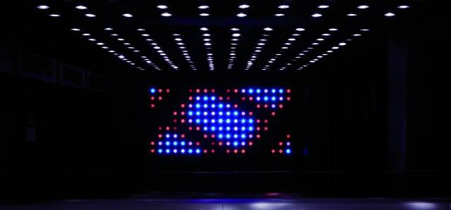 Een verlichte plafond met rijen blauwe en rode lichten die een geometrisch patroon vormen in een donkere ruimte.