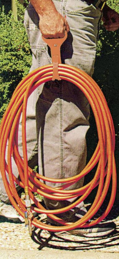 Een persoon houdt een opgerold, oranje verlengsnoer naast een struik in de tuin.
