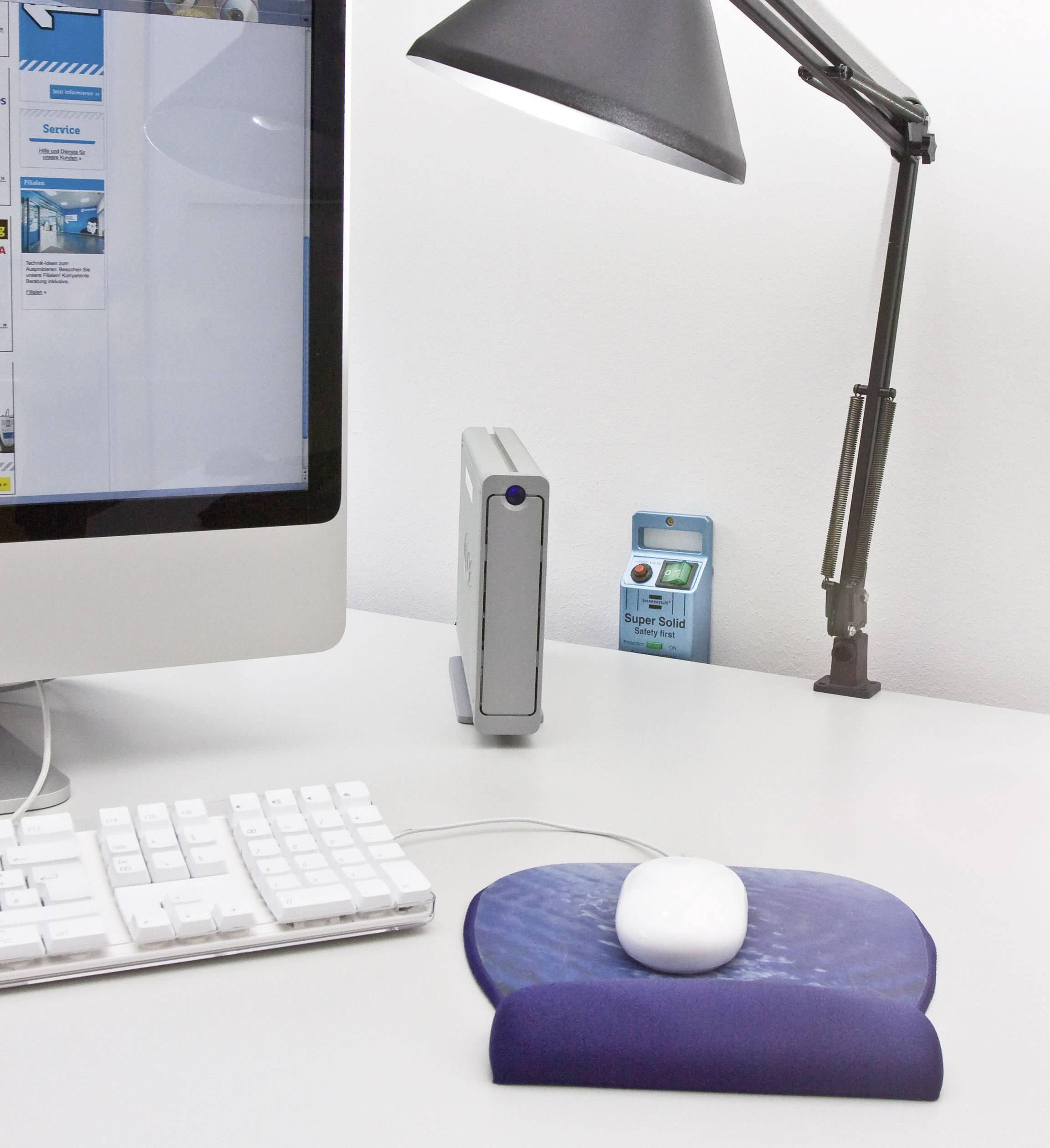 Een bureau met een computer, een toetsenbord en een muis op een blauw muismat. Een lamp staat rechts naast de muis.