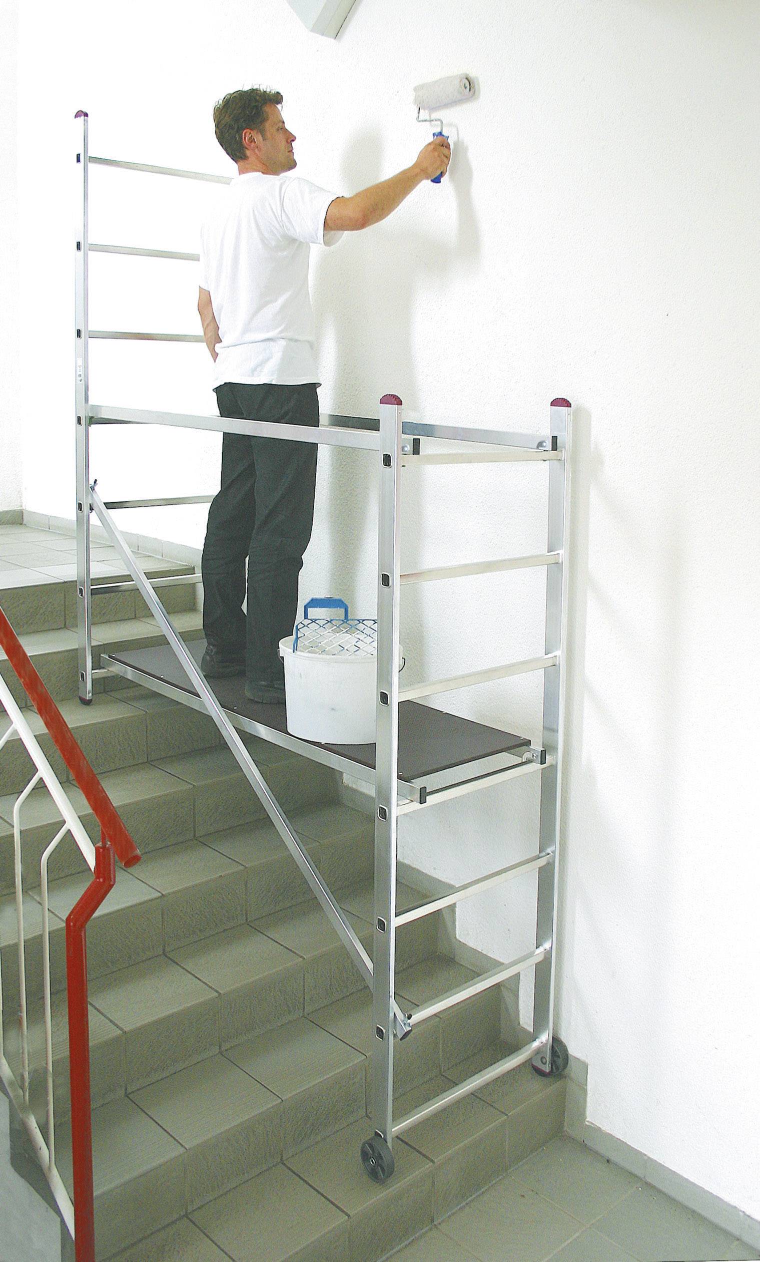 Een man schildert met een verfroller een witte muur, staande op een ladder die op een trap is geplaatst.