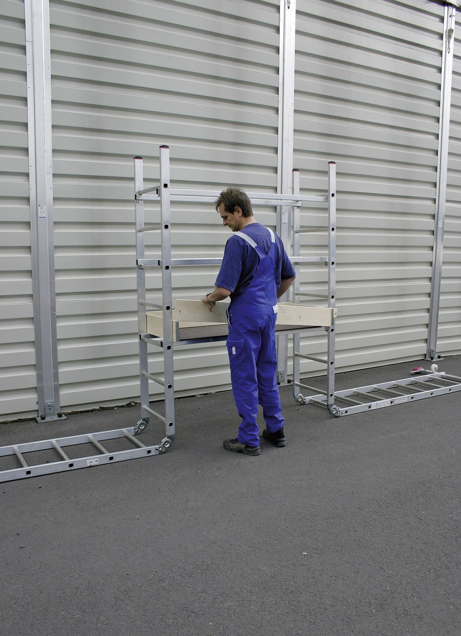 Een persoon in blauwe werkkleding staat op een steiger voor een grijze gegolfde metalen muur, geconcentreerd aan het werk.