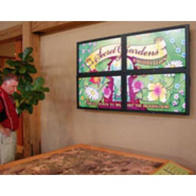 Een persoon bekijkt een digitaal scherm met een kleurrijke poster voor 'Arboretum Gardens' in een binnenruimte met een plant en een tafel.
