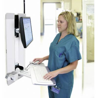 Een vrouw in ziekenhuiskleding staat aan een computerworkstation, typt op het toetsenbord en kijkt naar het scherm.