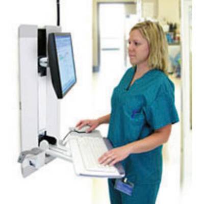 Een persoon in medische kleding werkt aan een wandcomputer in een ziekenhuisgang. Ze typt op een toetsenbord.