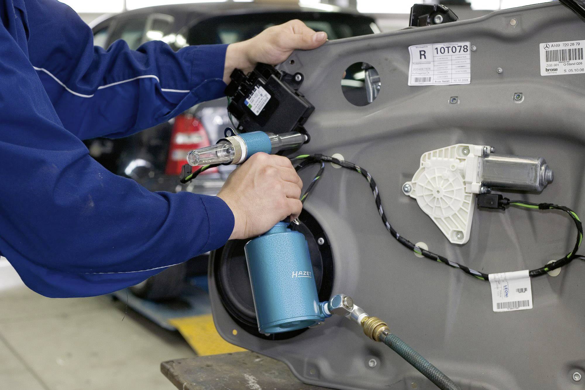 Een persoon repareert een autodeel in een werkplaats. De handen houden gereedschappen vast en zijn gericht op een binnendeur van een auto.