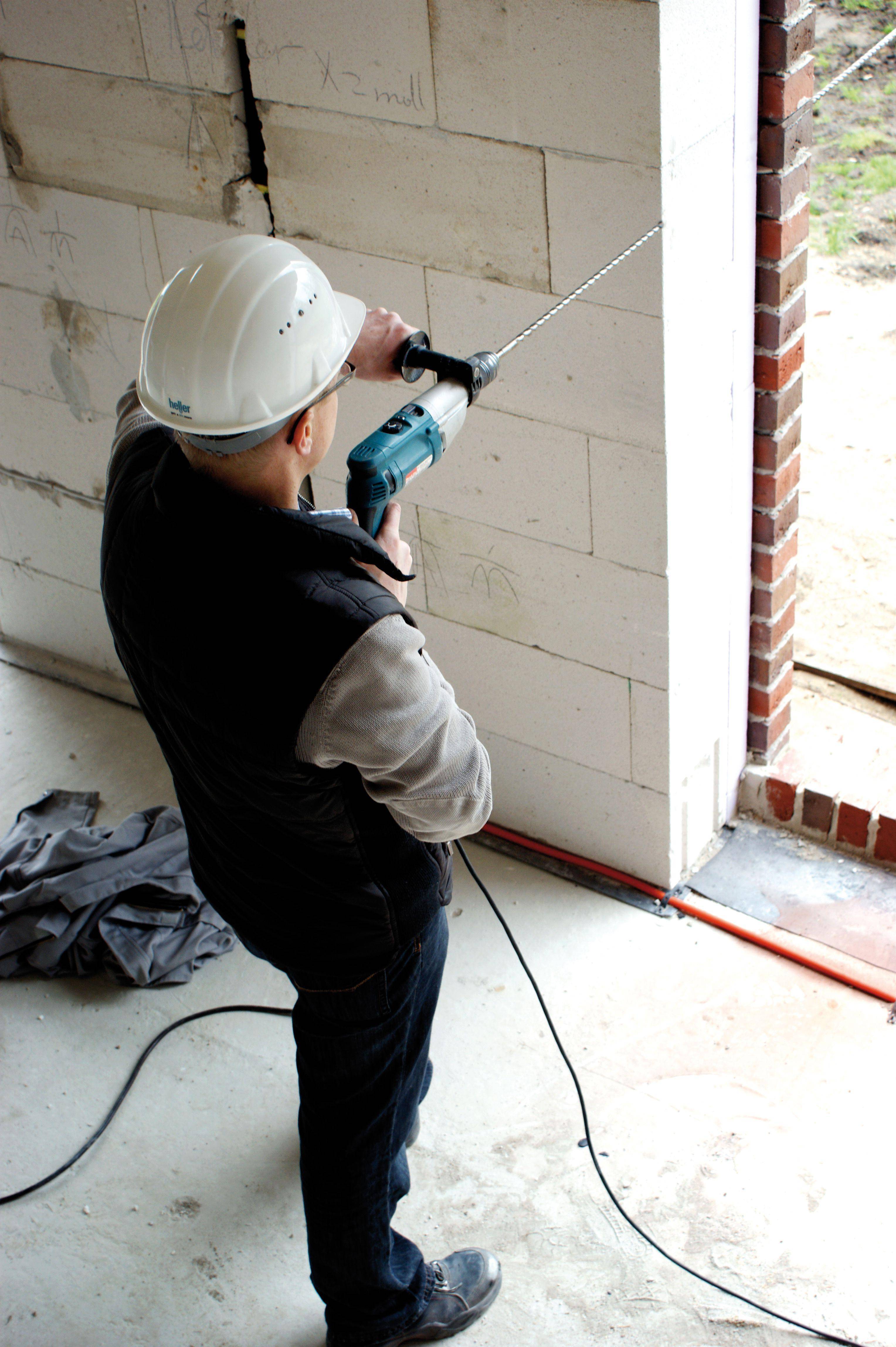 Arbeider met veiligheidshelm gebruikt boormachine aan muur op bouwplaats.
